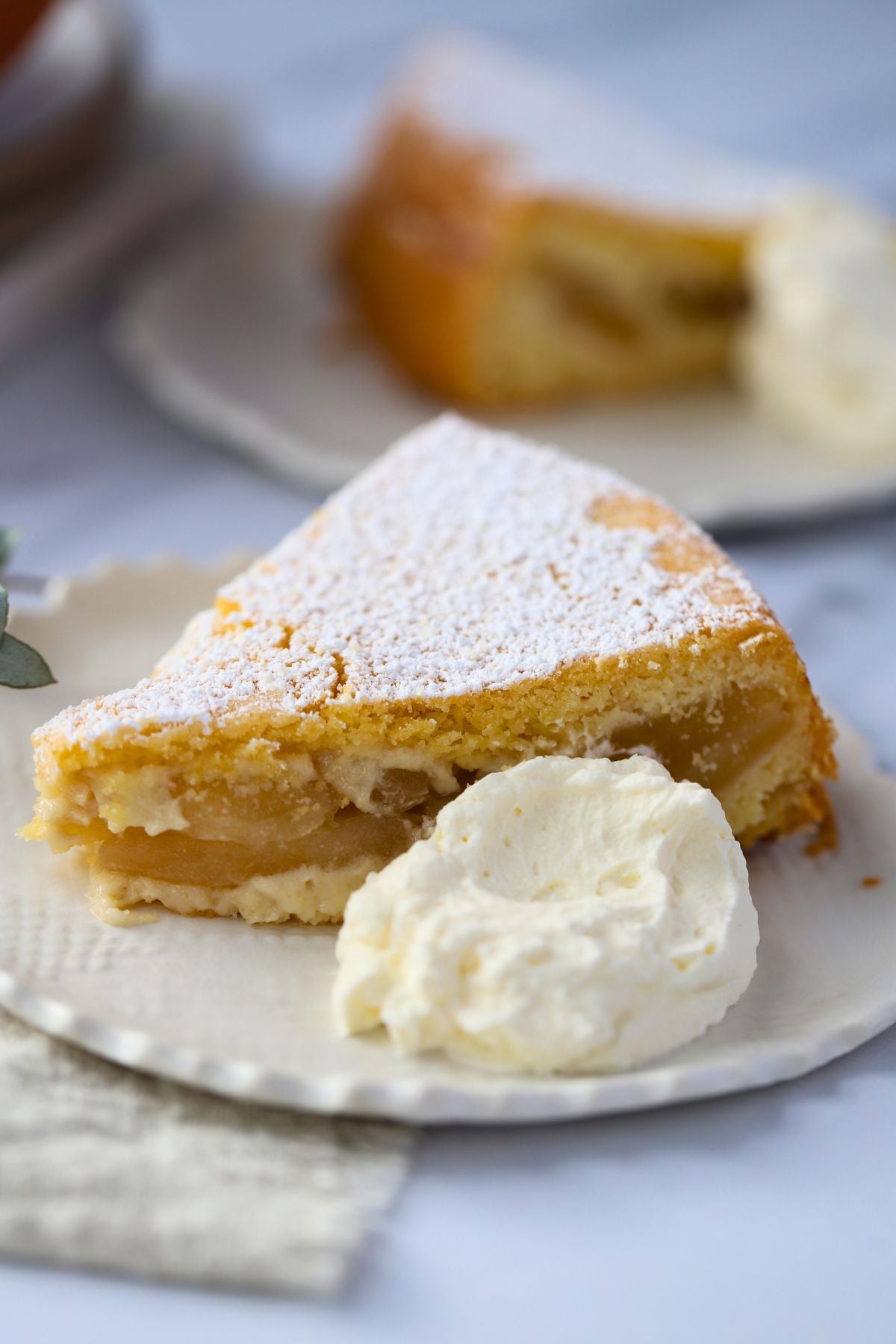 piece of apple cake on a small plate with a dollop of whipped cream to the side of the cake. A second plate of cake is behind the front.