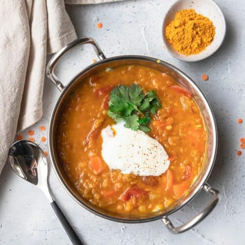 red lentil dal in a small metal dish with a spoon and dish of turmeric