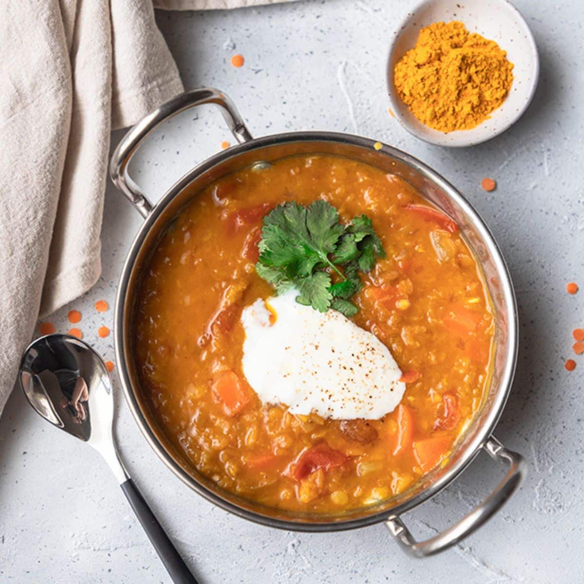 red lentil dal in a small metal dish with a spoon and dish of turmeric