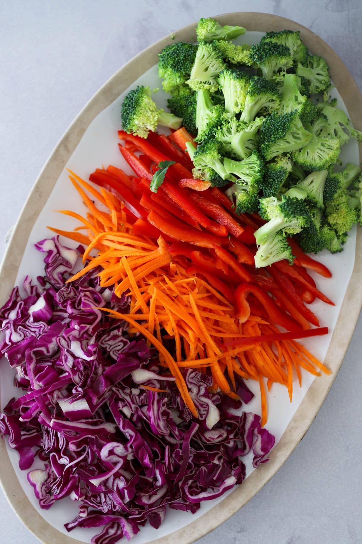 soba noodle salad ingredients on a plate from top to bottom - broccoli, red pepper, carrot and purple cabbage