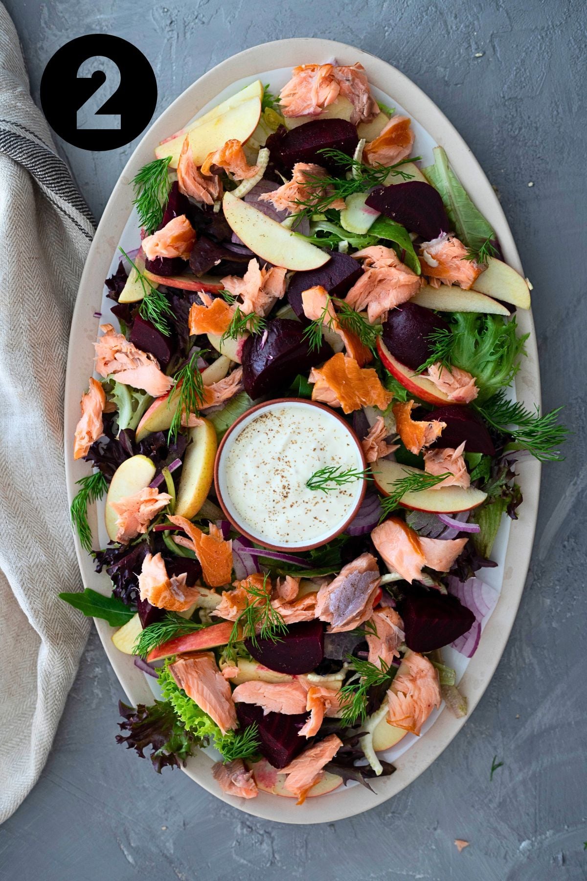 all the smoked salmon salad ingredients on a large platter. A bowl with the horseradish cream sits in the middle of the salad.