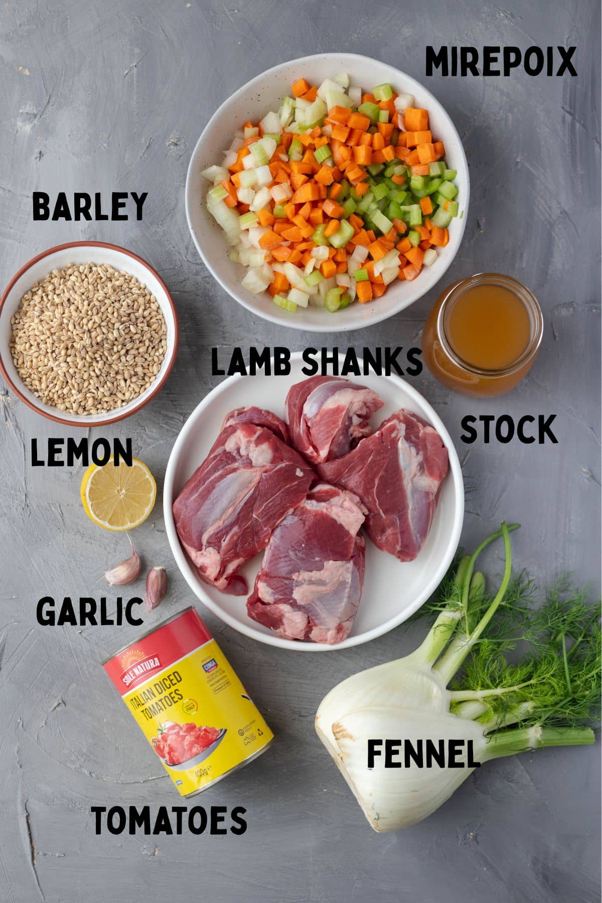 Lamb shank soup ingredients on board from top to bottom - mirepoix, barley, stock, lamb shanks, lemon, garlic, fennel and tomatoes.