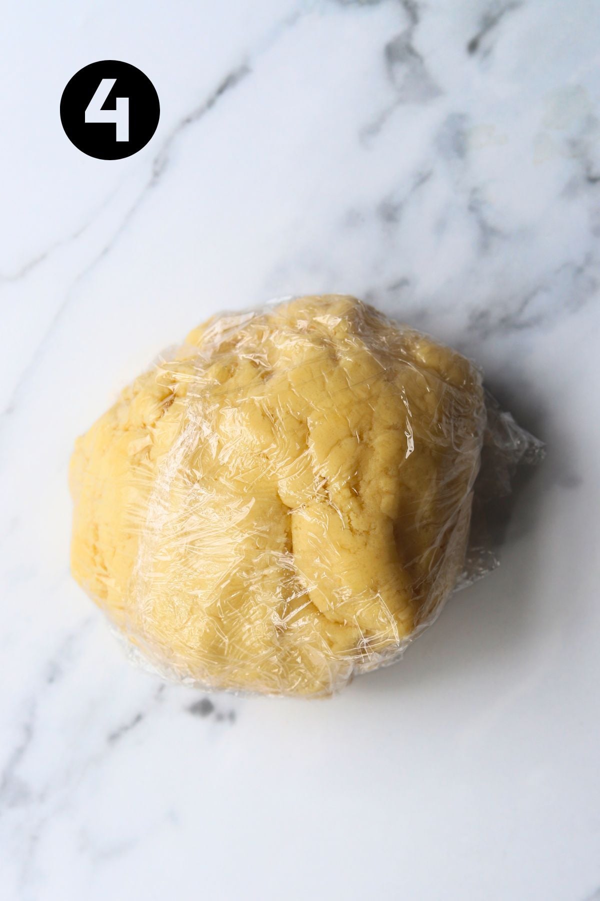 dough wrapped in plastic wrap on marble board.