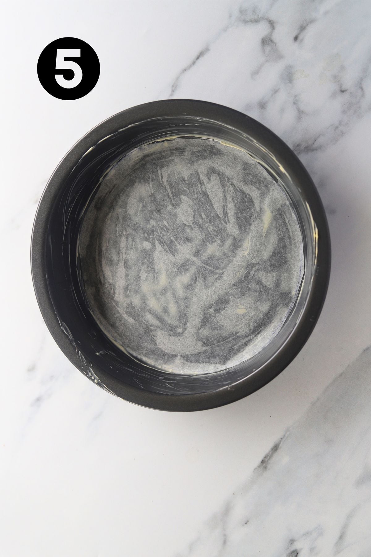 9 inch / 23 cm cake tin on a marble board. Cake tin has been greased, and parchment paper cut into a circle to fit the bottom of the tin.