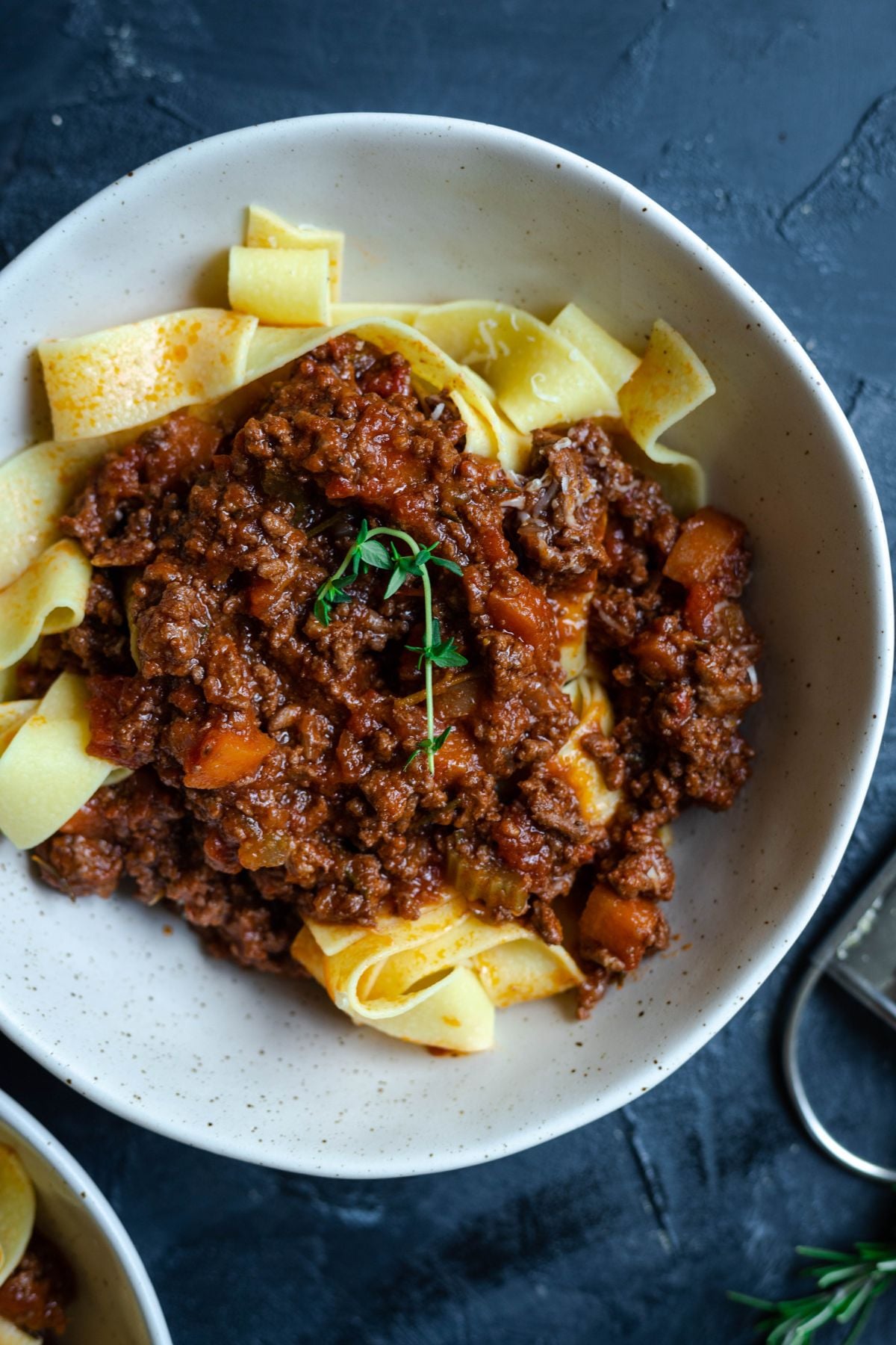 lamb ragu on top of a bowl of pappardelle pasta. there is a sprig of time on top of the meat sauce.