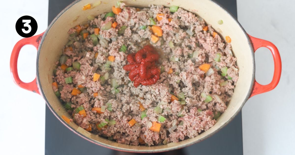 tomato paste added to lamb mixture in a dutch oven on portable stove top.