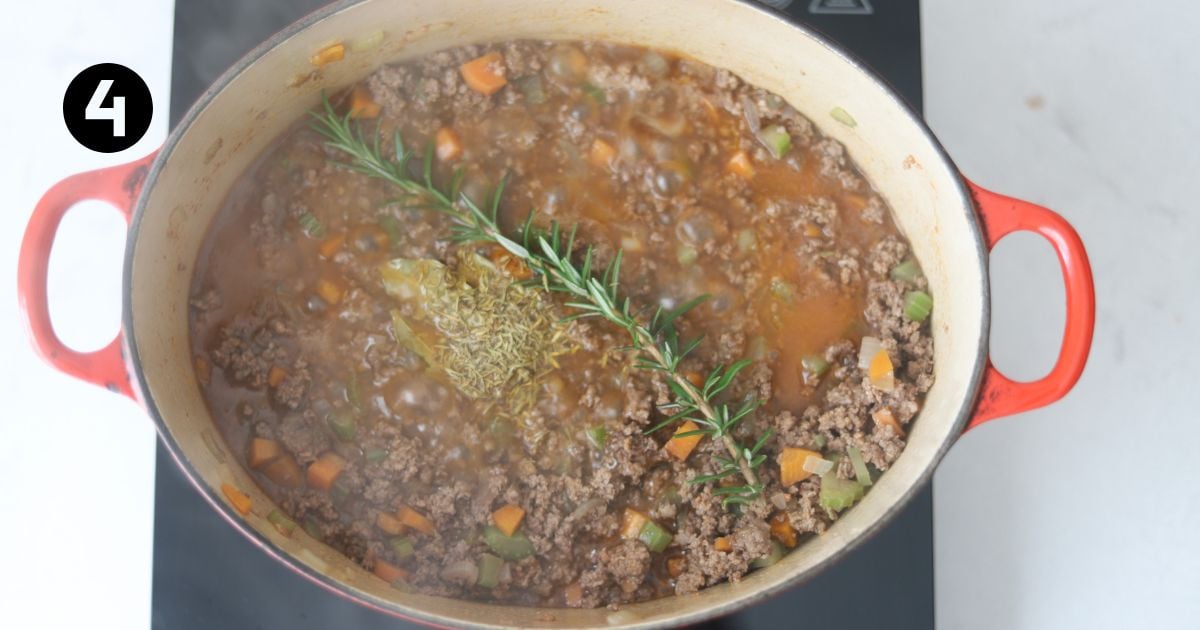 herbs added to meat sauce in a dutch oven on portable stove top.