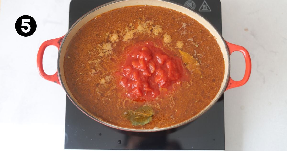 tin tomatoes added to meat sauce in a dutch oven on a portable stove top.