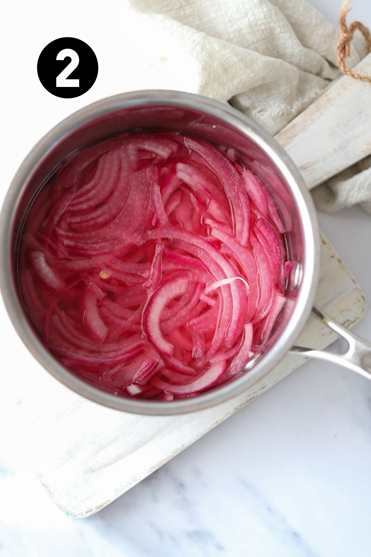 finished pickled onions in a saucepan on a board with a linen towel.