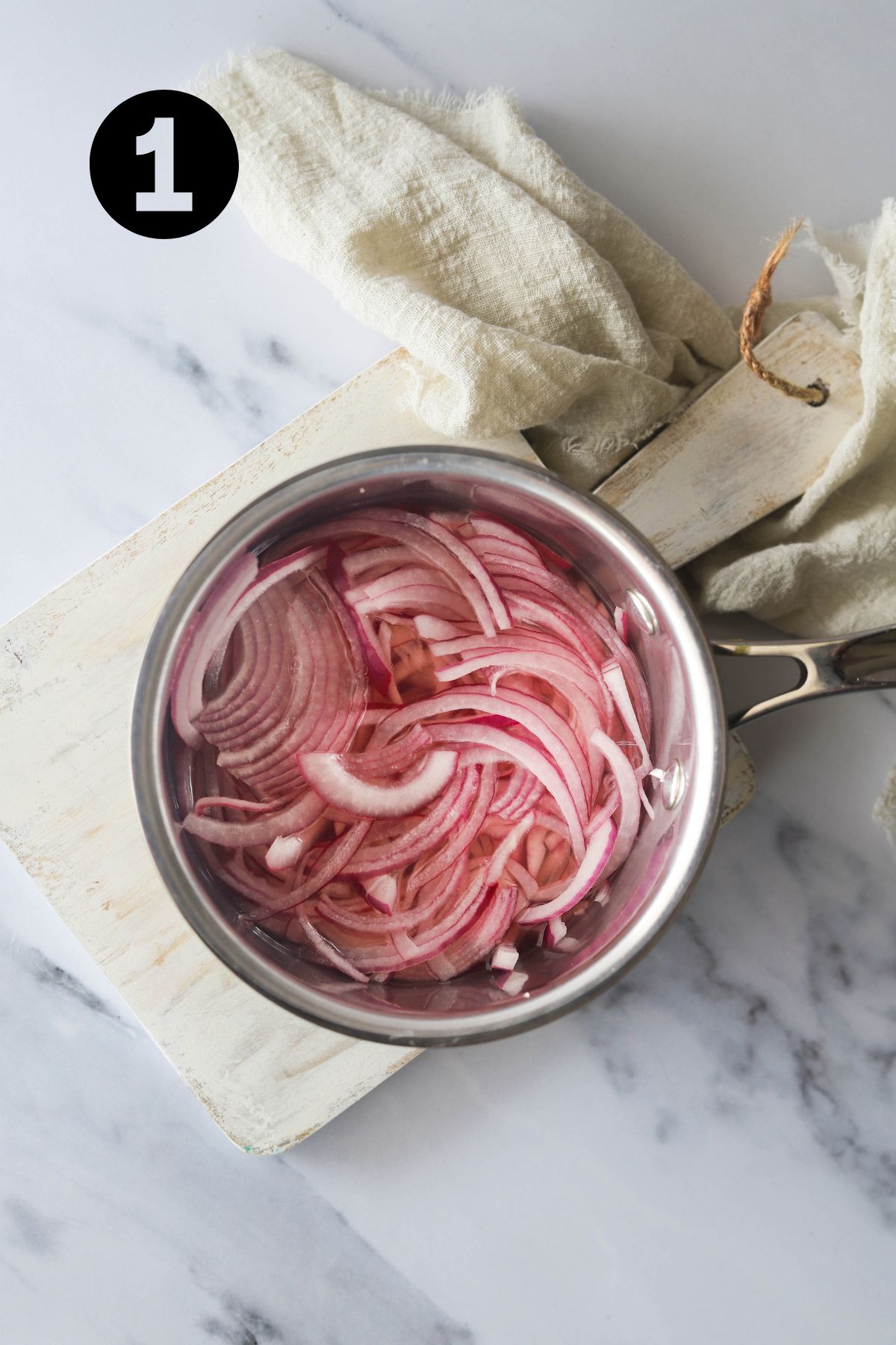 raw red onions in a saucepan on a board with a linen cloth.