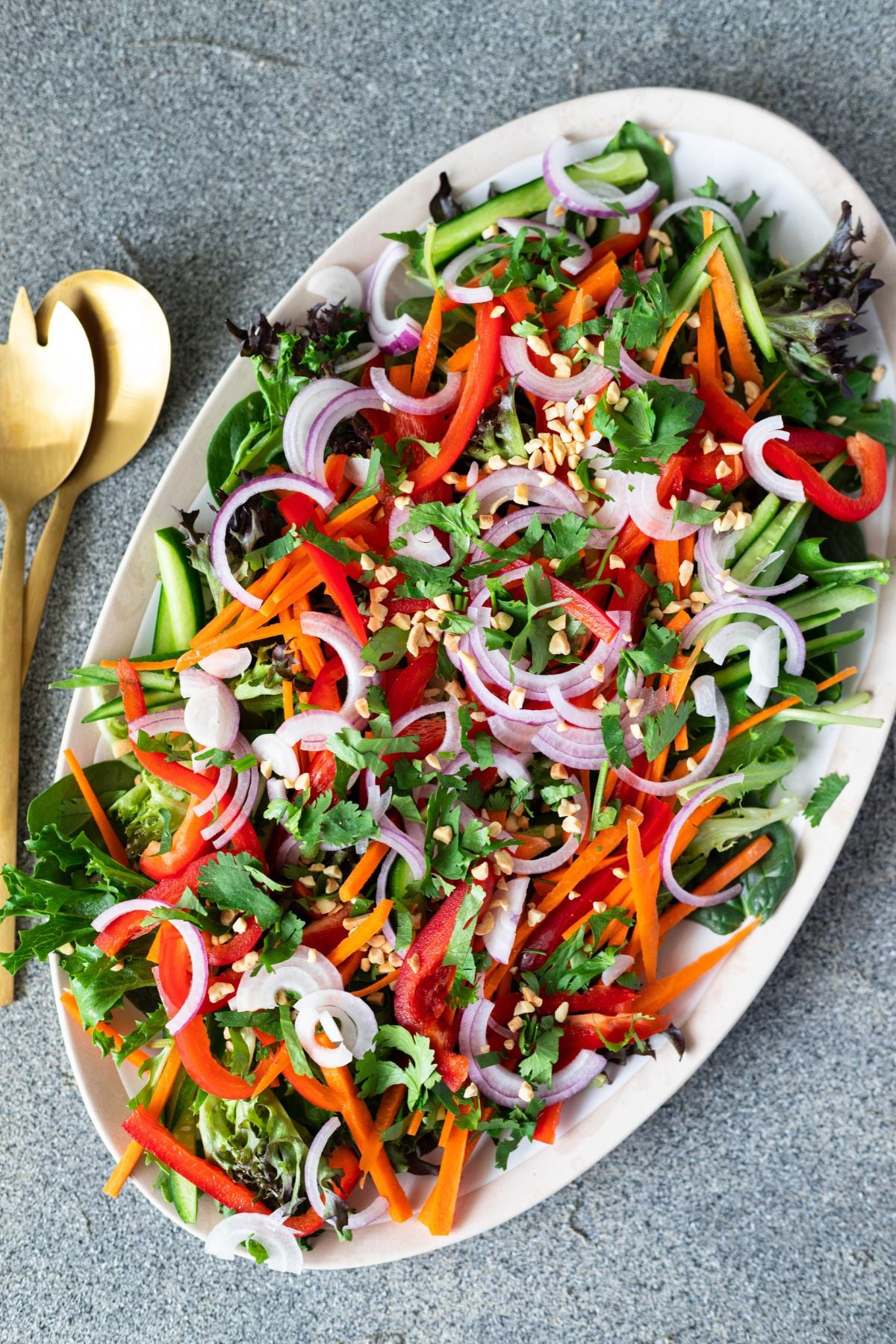 thai salad on a large oval platter. there are salad servers on the side. the salad is topped with peanuts and onions.
