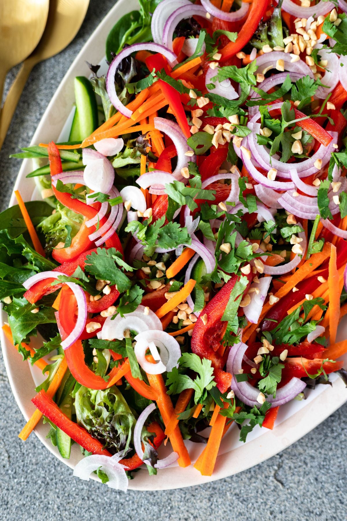 half a platter filled with the Thai Salad. there are salad servers in the corner on the board.
