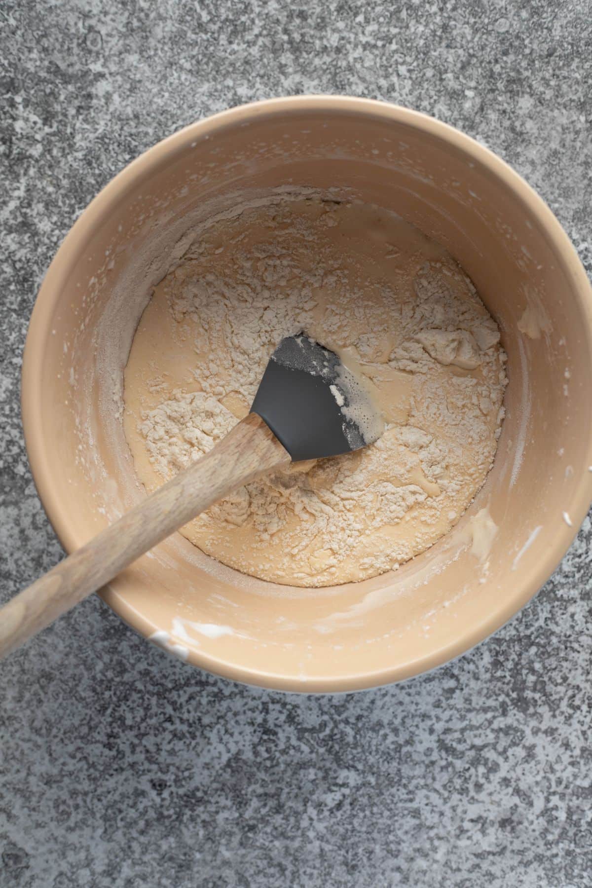 a mixing bowl with cake ingredients and mixed flour. A spatula sits in the mixing bowl.