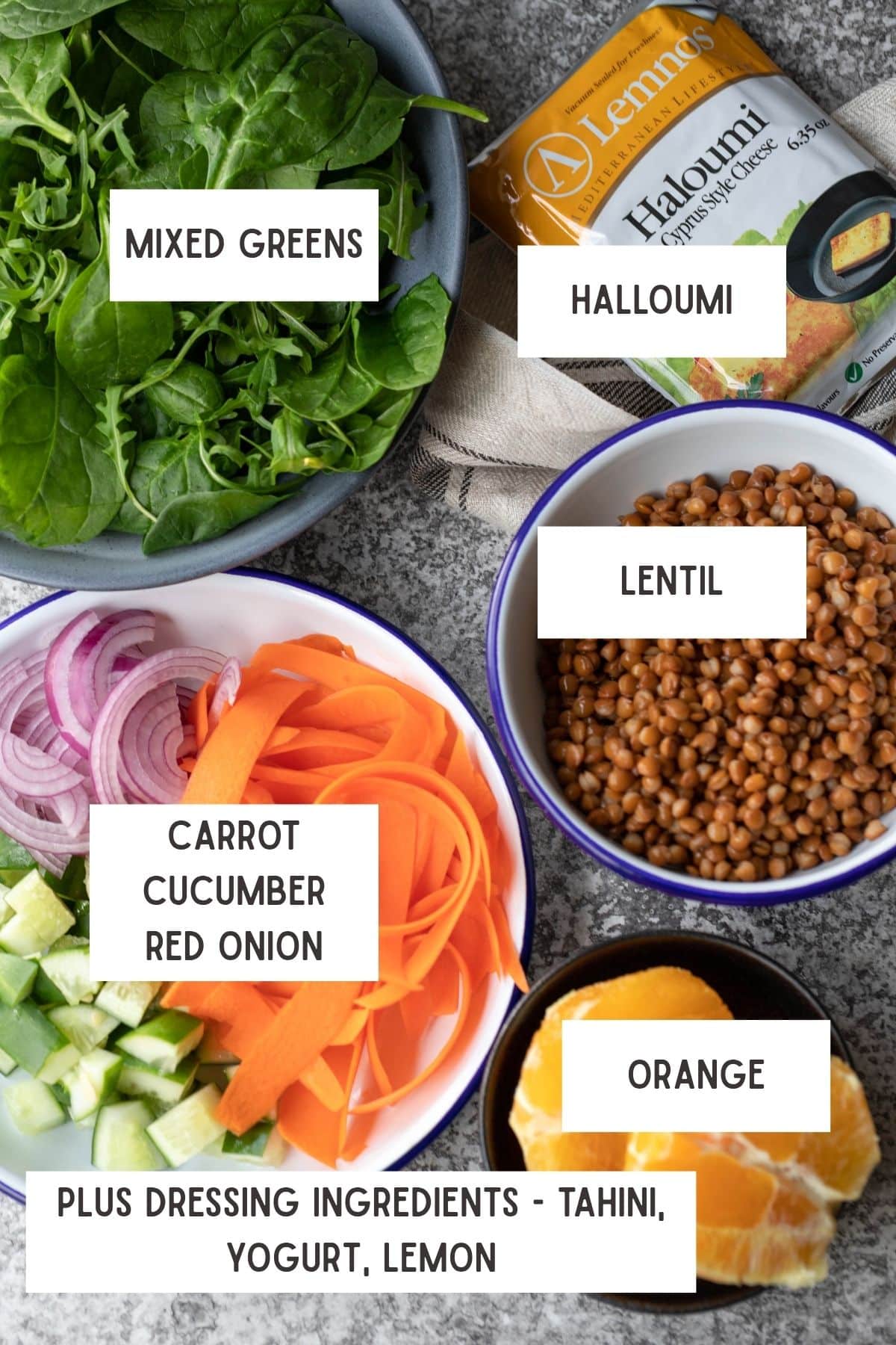 salad ingredients laid out on board. From top to bottom, left to right - mix greens, halloumi, bowl of cucumber, carrot and red onion, bowl of lentils, bowl of orange.
