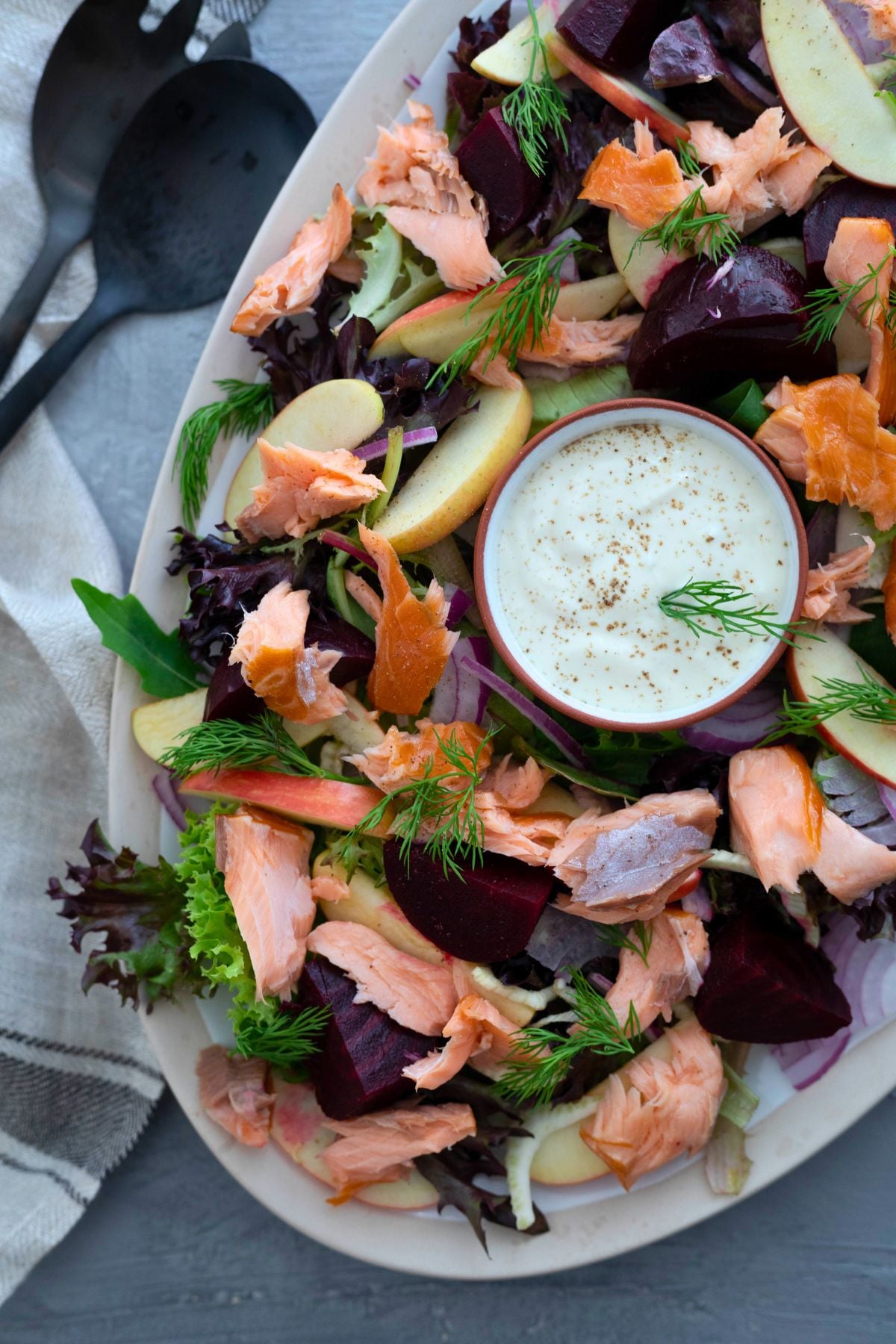 hot smoked salmon salad on a large platter. A pair of salad servers are to the left of the platter.