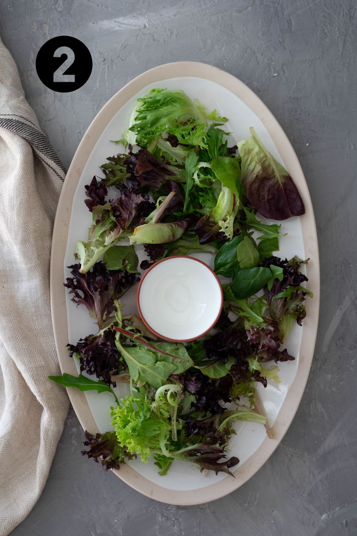 salad greens on large platter. in the middle of the plate is a small empty bowl.
