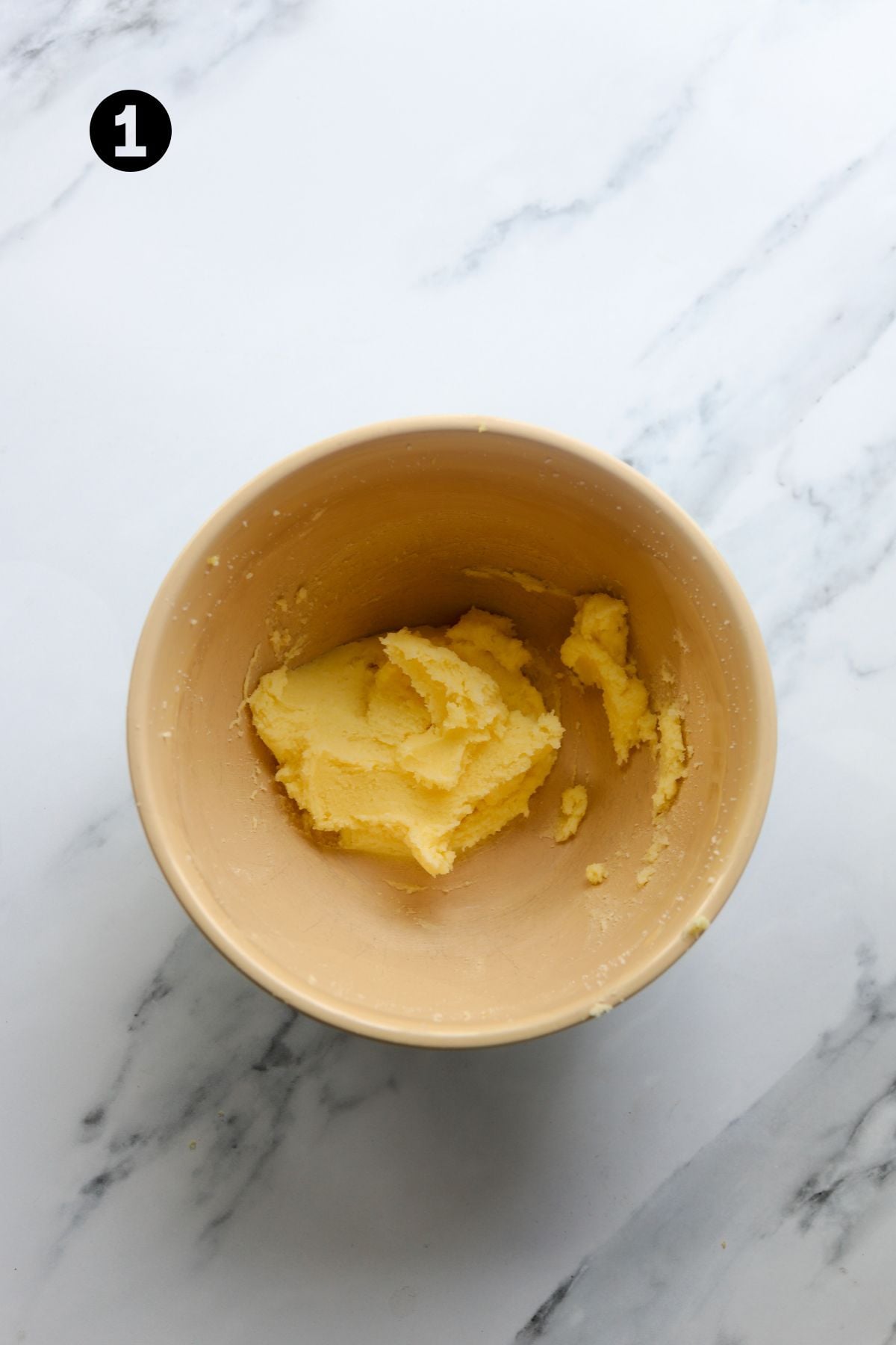 butter and sugar mixed together in a large bowl on a marble board.