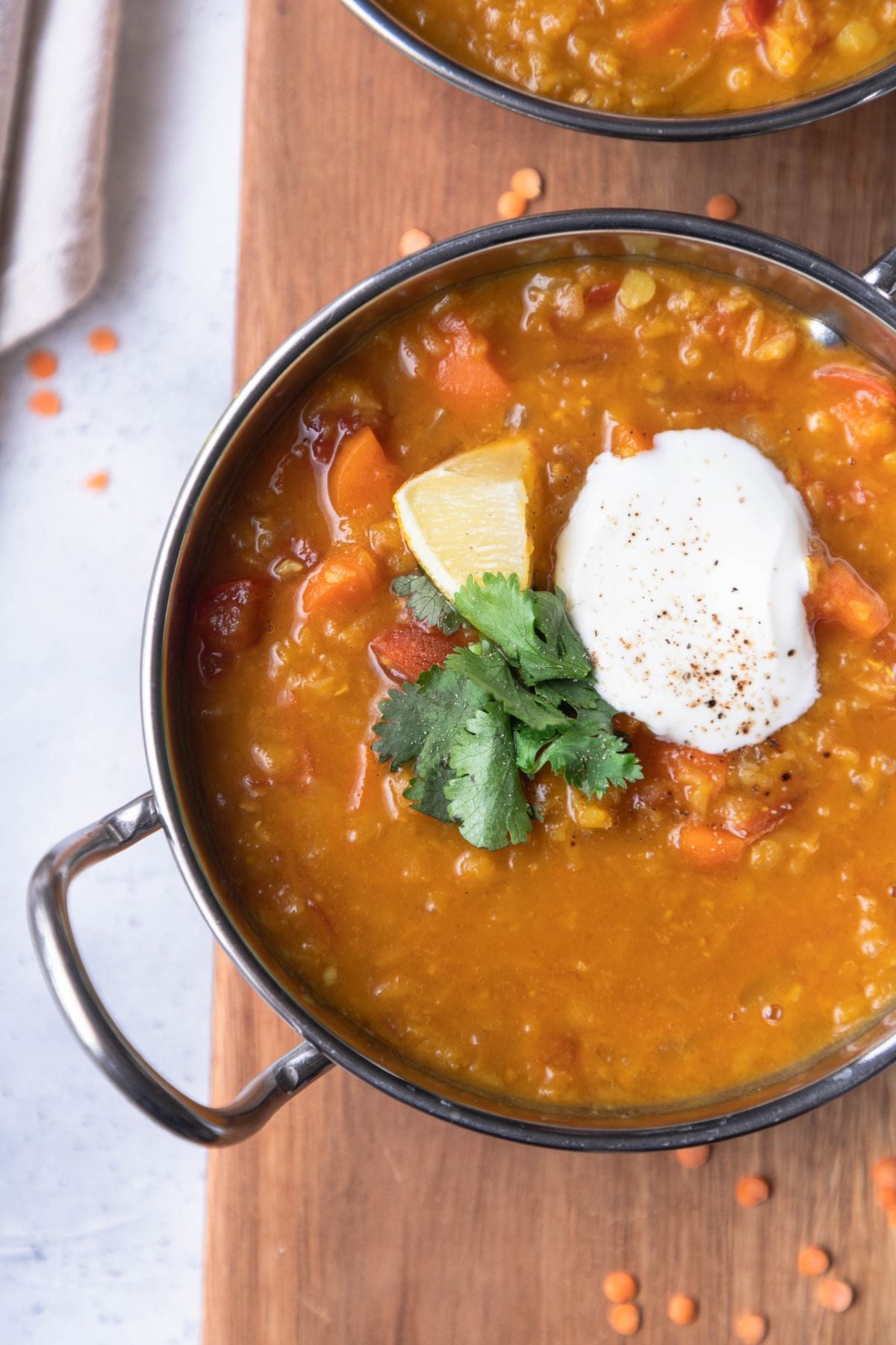 Red lentil dal in a stainless steel bowl. Yogurt, cilantro and lemon are on top of the dal.
