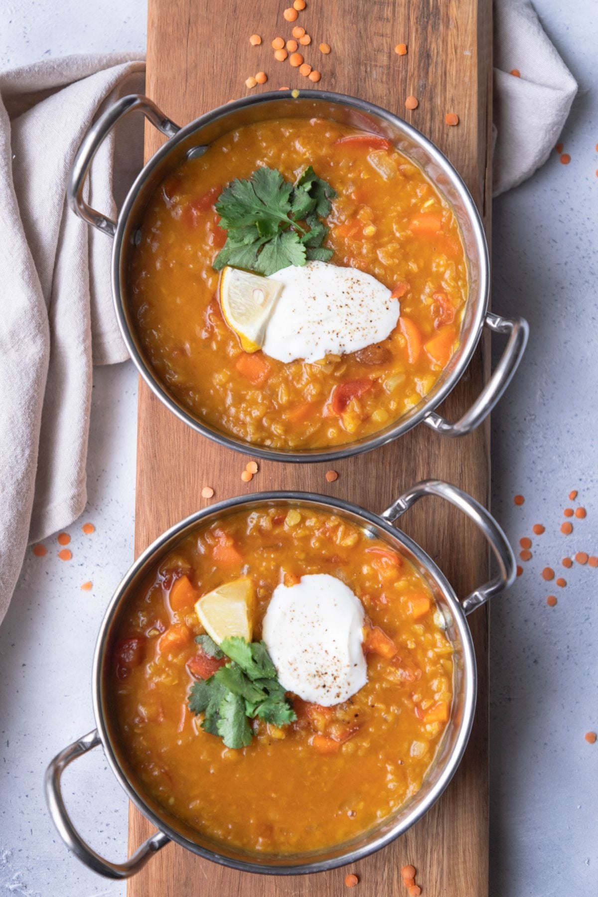 Two bowls of lentil dal on a long wooden board.