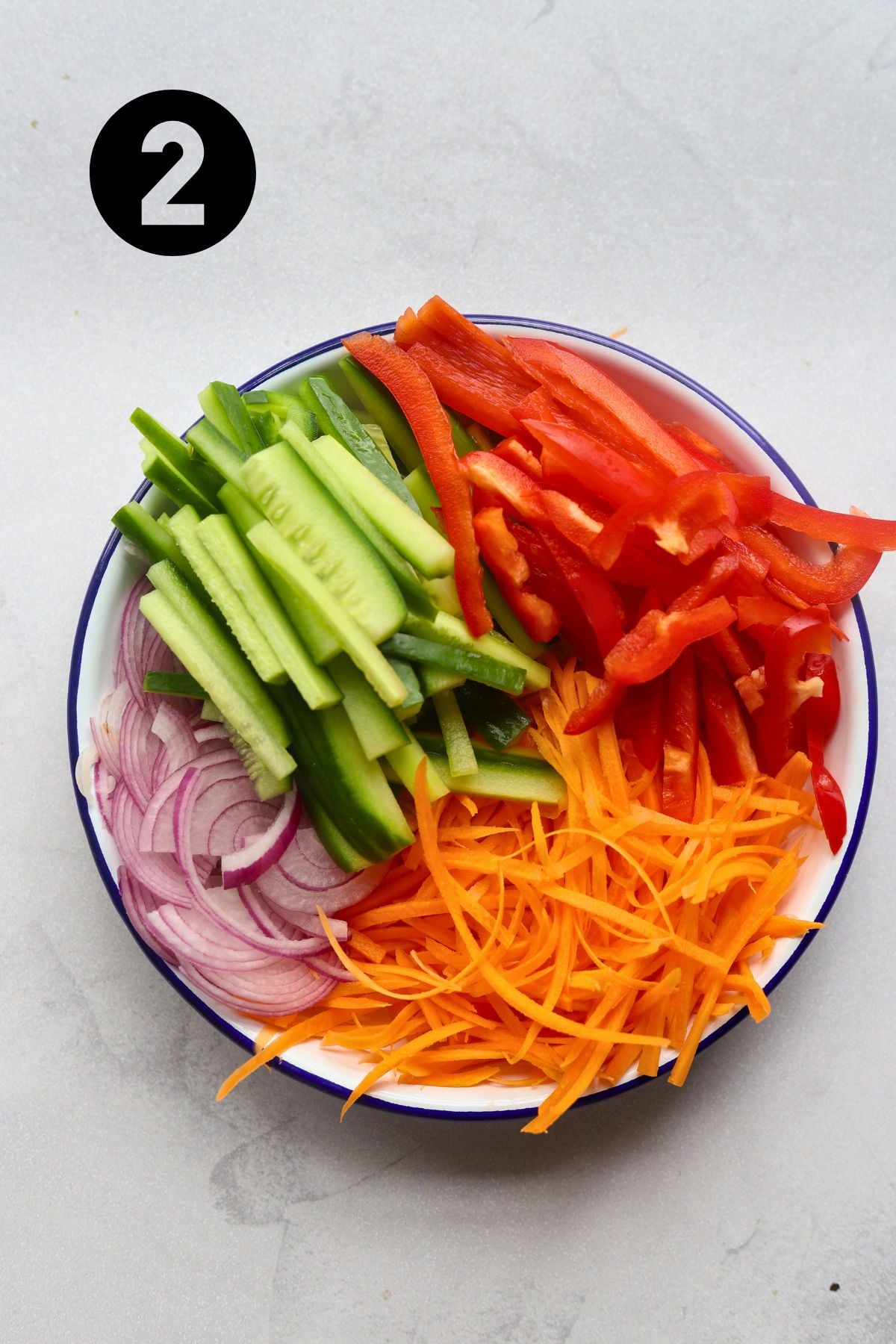 chopped cucumber, bell pepper, carrot and cucumber in an enamel bowl.