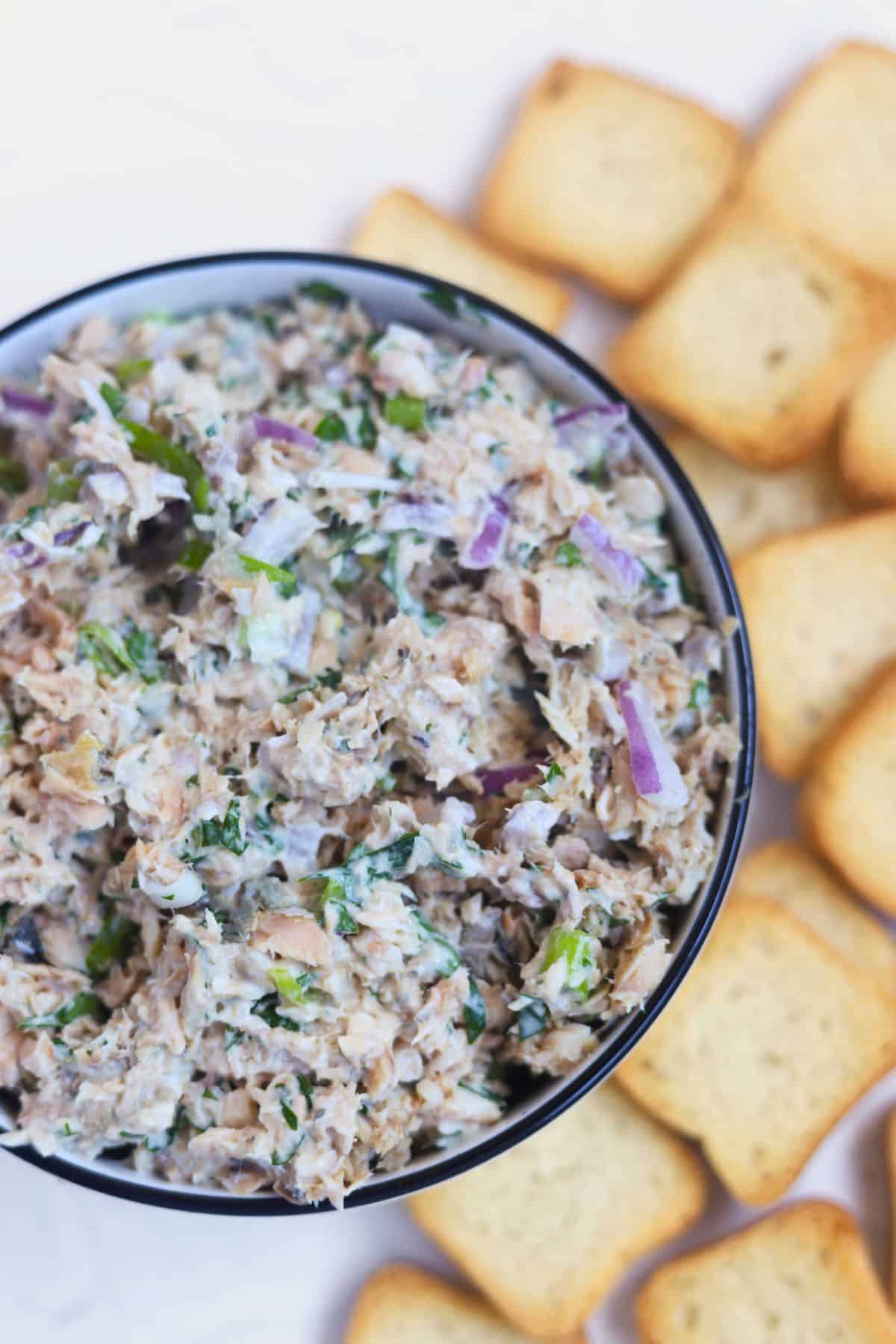 Close-up of salmon dip in a small bowl surrounded by mini toasts.