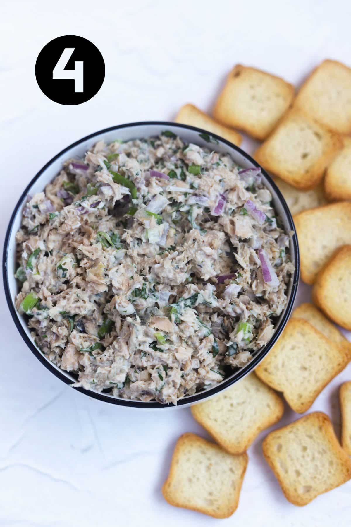 salmon dip in small bowl surrounded by mini toasts.